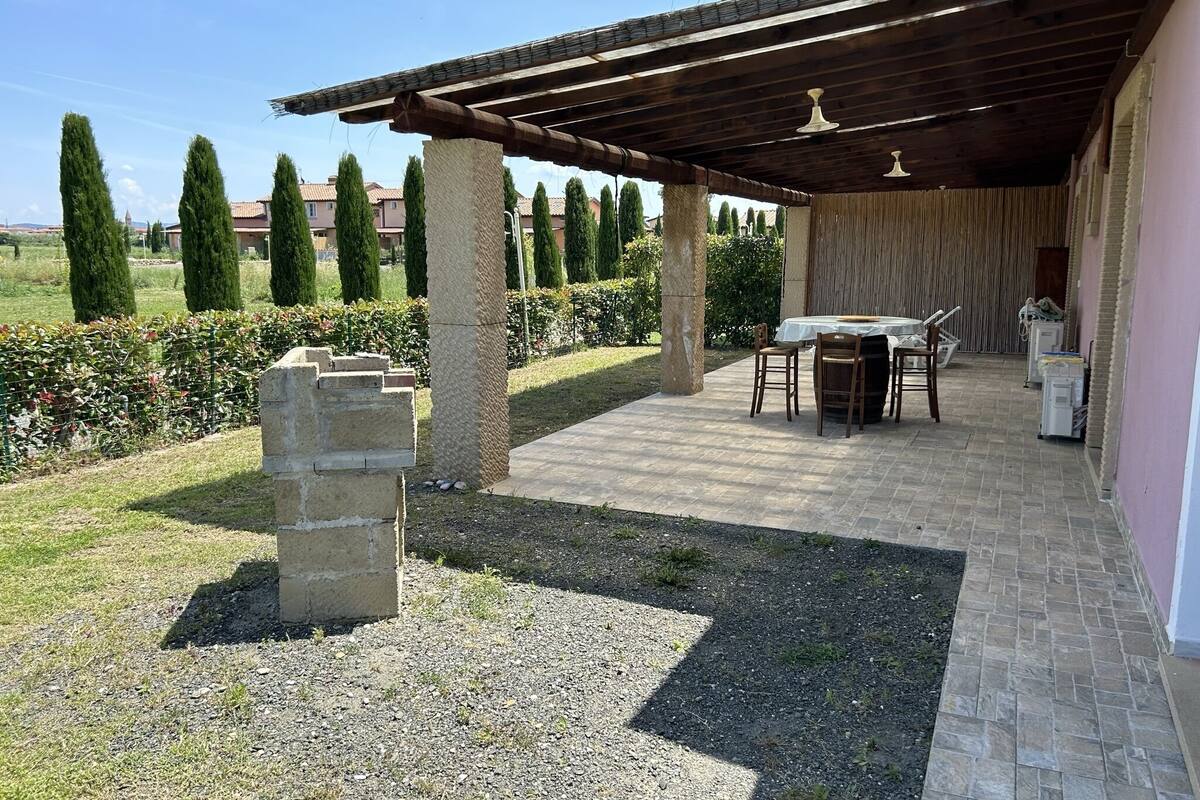 Un patio al aire libre con una pérgola, columnas de piedra y una mesa con sillas.
