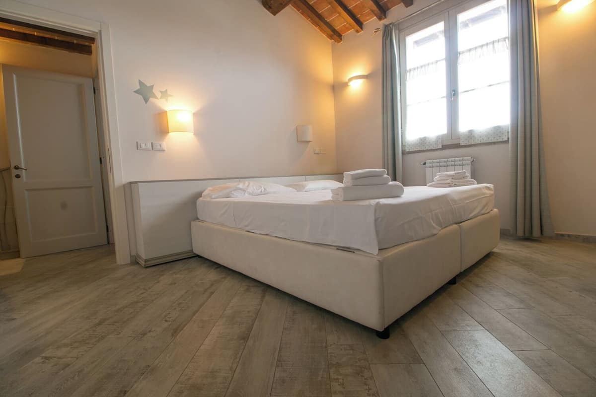 Un dormitorio con una cama grande, piso de madera, una ventana con cortinas y luces fijadas a la pared.