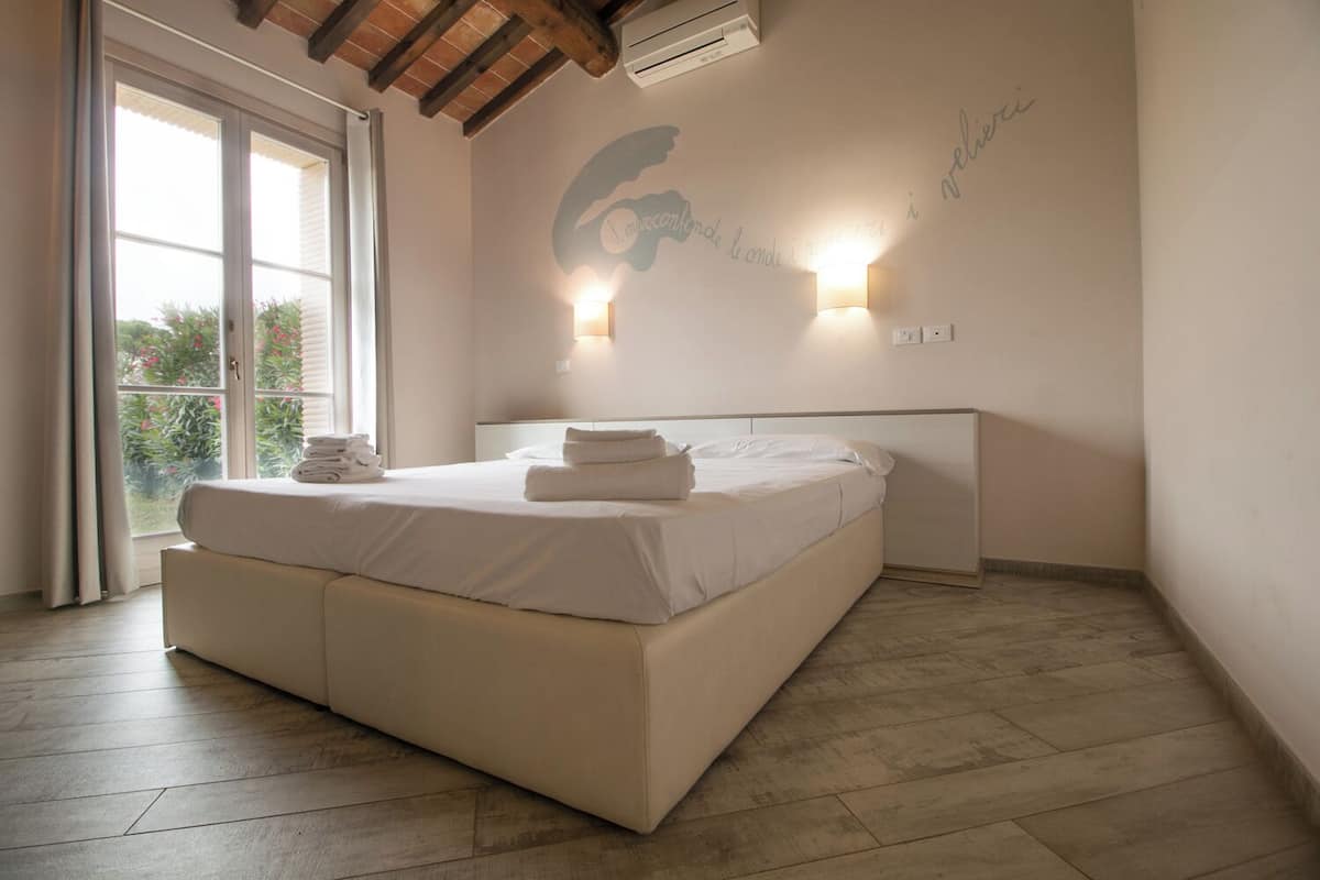 Un dormitorio con una cama grande, una ventana con cortinas, una lámpara de pared y un adorno en la pared.