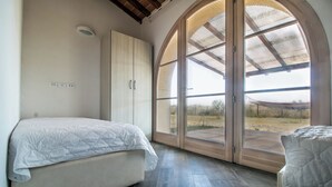 A bedroom with a bed, a wardrobe, and a large arched window. - Fattoria Palazzeta Pet & Family Friendly (Cecina)
