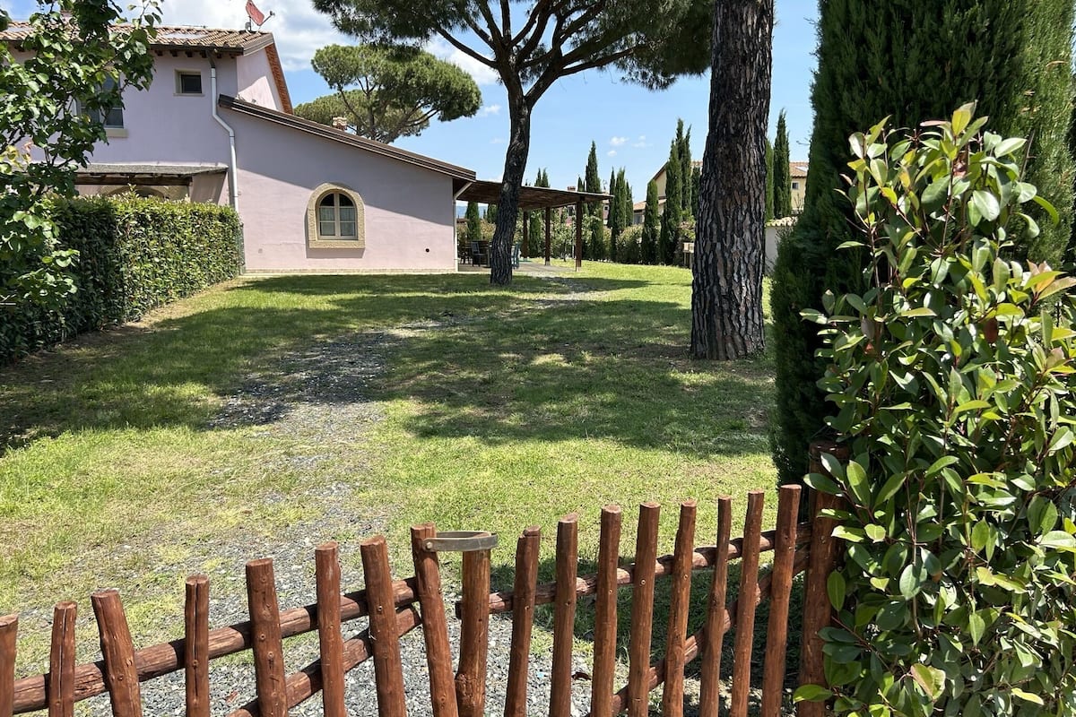 Una casa con entrada pavimentada, cerca de madera y césped bien cuidado.