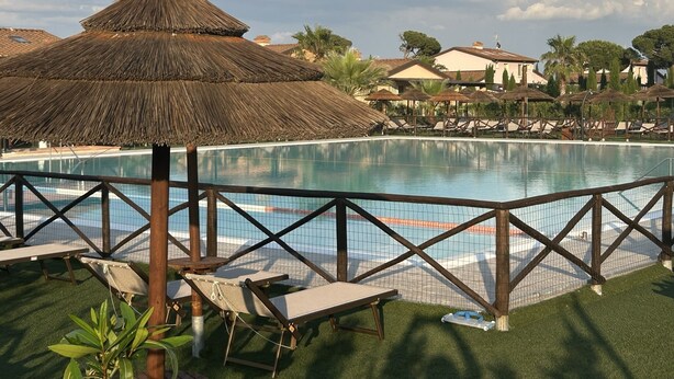 A pool area with lounge chairs and a thatched umbrella, surrounded by a fence and greenery. - Fattoria Palazzeta Pet & Family Friendly (Cecina)
