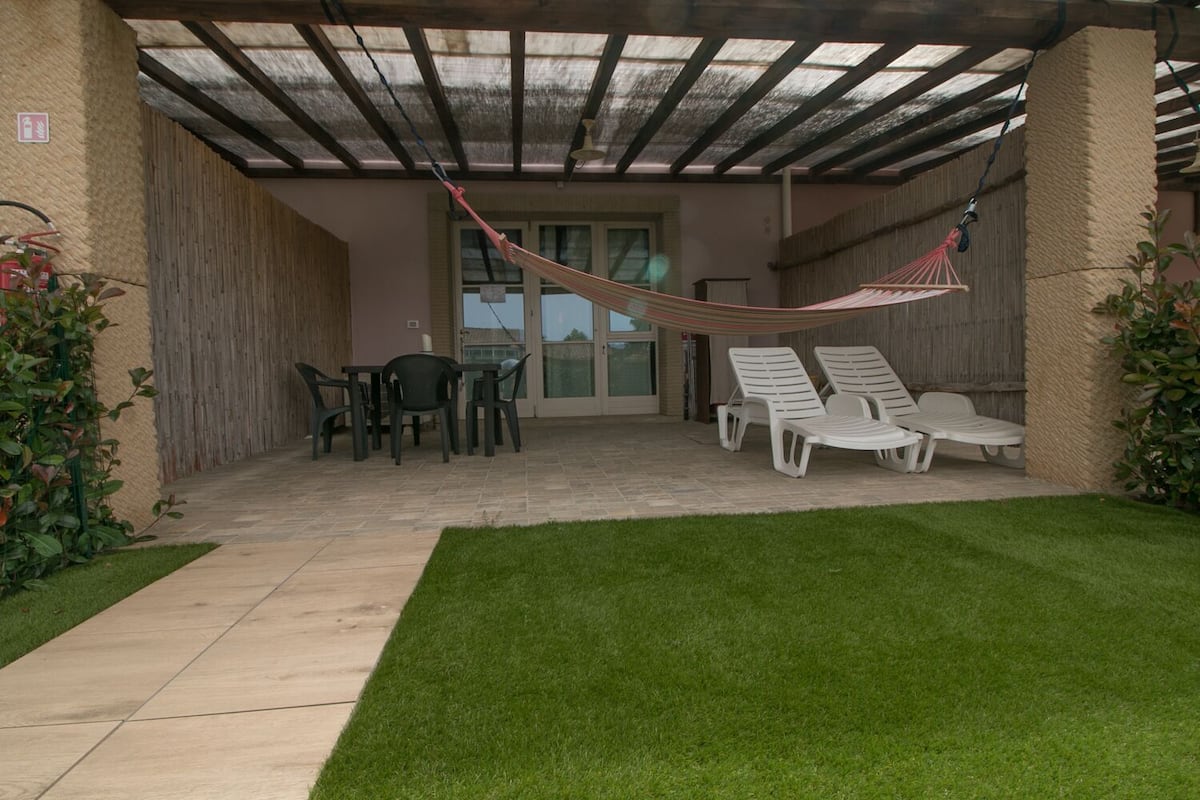 Un patio al aire libre con una mesa, sillas, una hamaca y una zona verde.