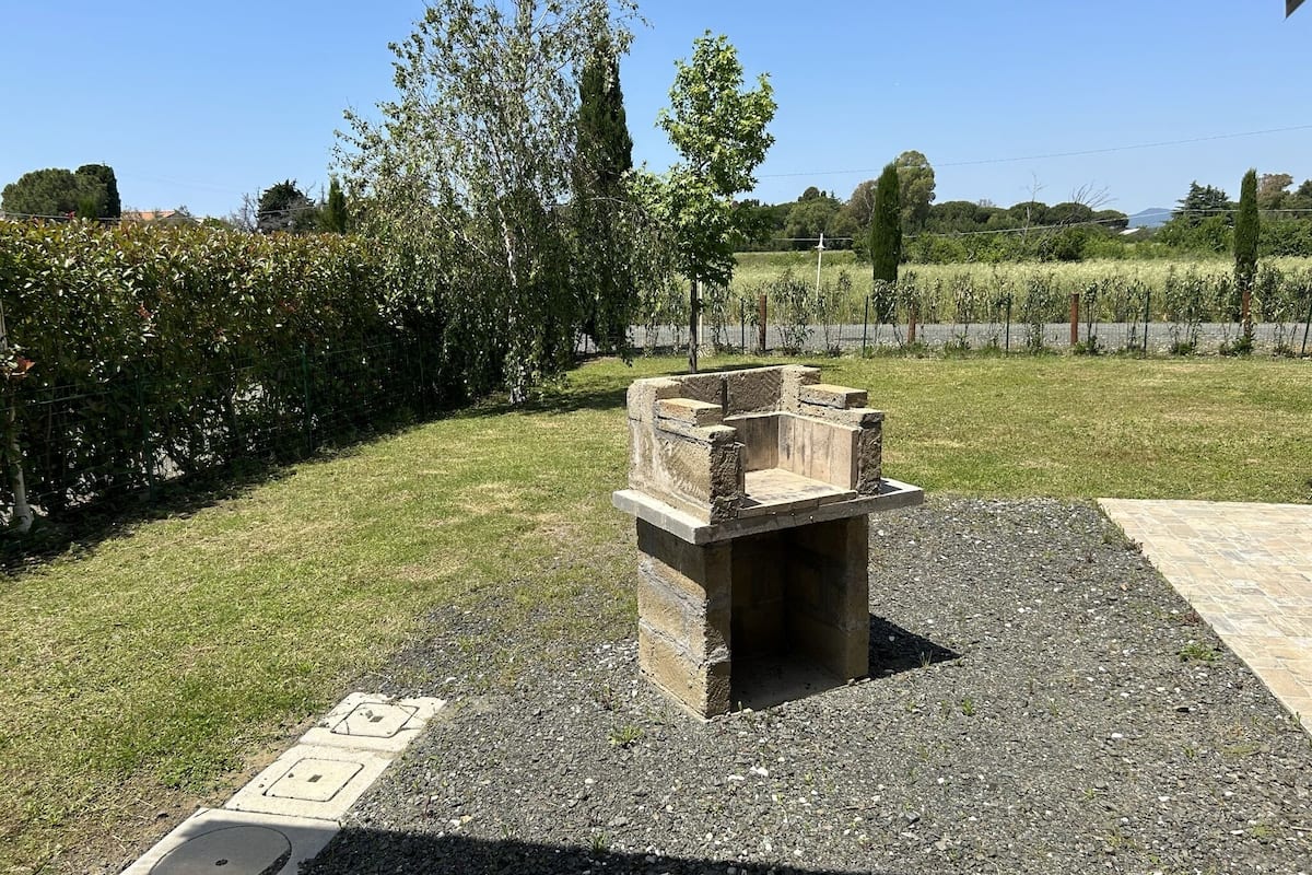 Una estructura de piedra al aire libre con una zona de estar, rodeada por un campo cubierto de césped y árboles.
