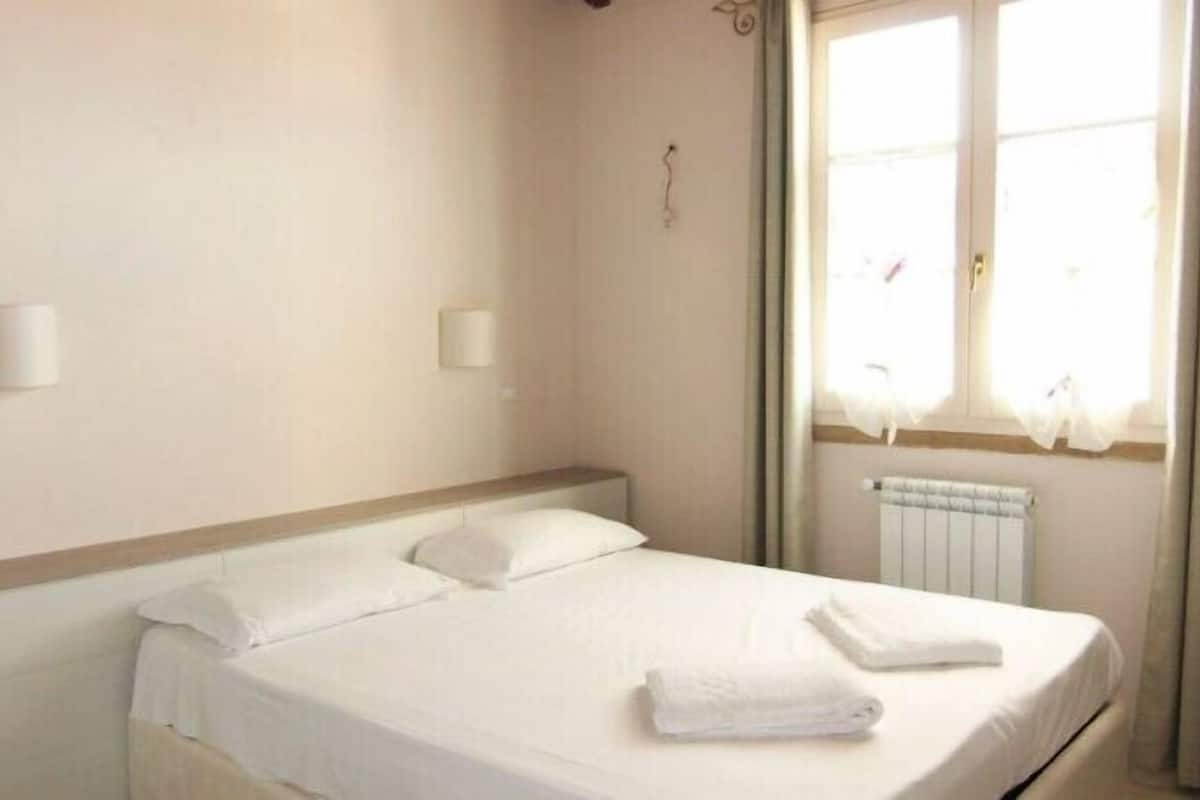 Habitación de hotel con una cama individual, una ventana con cortinas, un radiador y una pared decorada con dos estrellas.