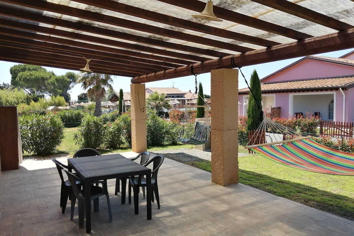 Un patio al aire libre con una mesa y sillas, una hamaca y una estructura de pérgola.