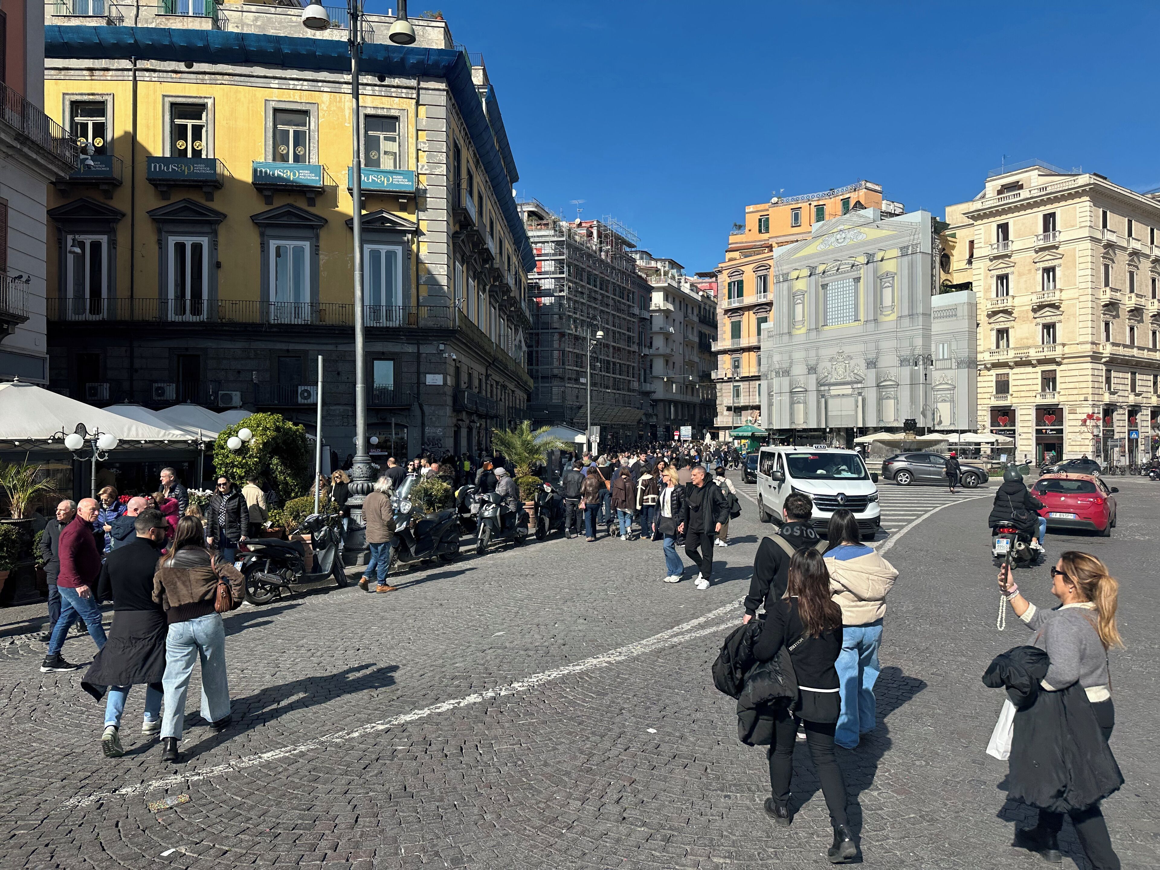 Une rue animée en plein centre-ville, où l’on croise des piétons, des scooters et des voitures.