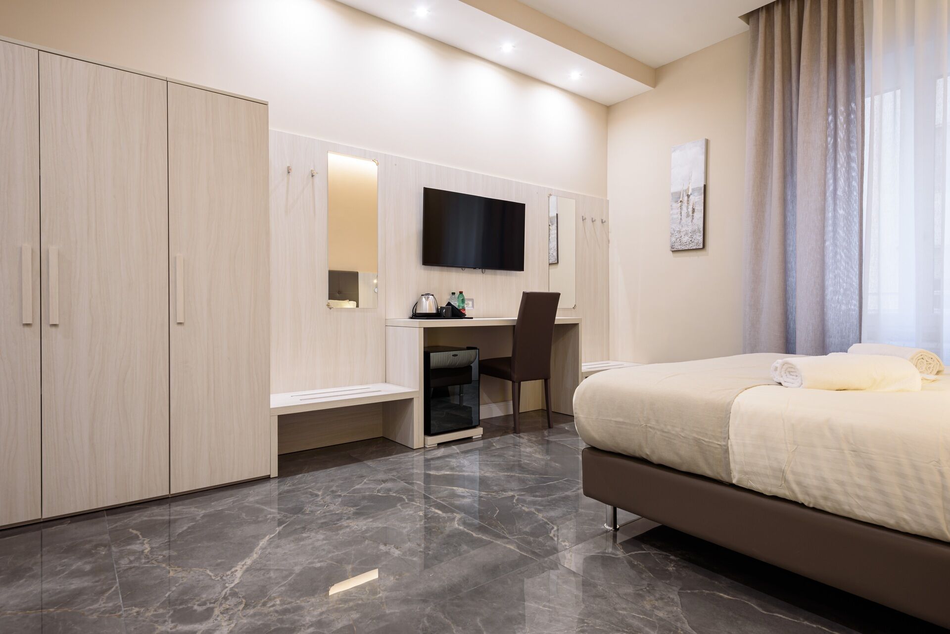 A modern hotel room with a bed, a desk, and a wardrobe.