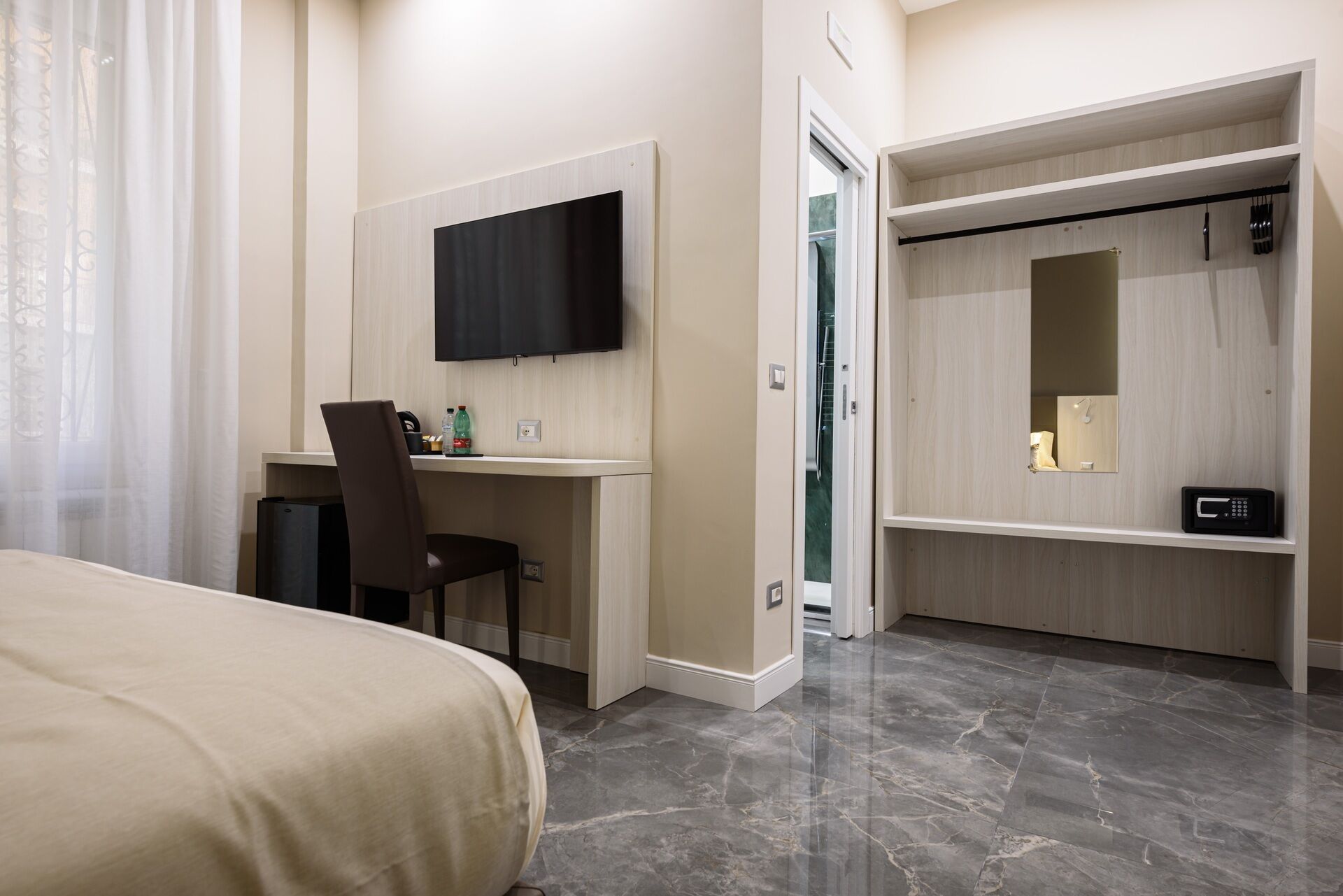 A hotel room with a bed, a desk with a chair, a television, a wardrobe, and a bathroom visible through an open door.