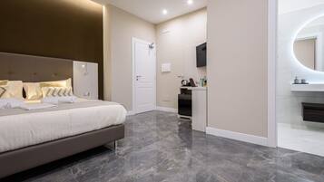 Quarto moderno com cama grande, armário embutido, pequeno espaço de cozinha e banheiro com espelho e vaso sanitário.