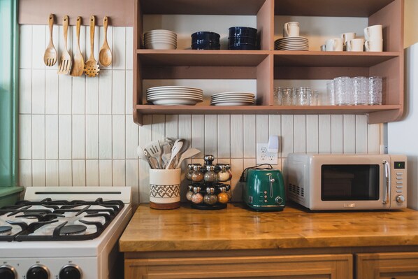 A kitchen with a stove, microwave, and shelves with dishes and utensils.