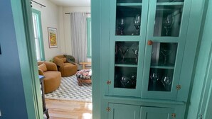 Un meuble de couleur turquoise avec des portes en verre, contenant des verres à vin, un tapis à carreaux et un canapé marron en arrière-plan.