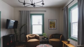Un salon chaleureux avec deux fauteuils, un téléviseur à écran plat, une cheminée et une grande fenêtre avec des rideaux.