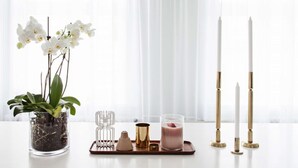 Zona pranzo con tavolo bianco, un lampadario, orchidee bianche, candele e un vassoio con portacandela e bicchiere.