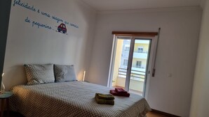 A bedroom with a bed, pillows, a nightstand, and a wall with a quote and a car illustration. - Praia da Saude (Setúbal)