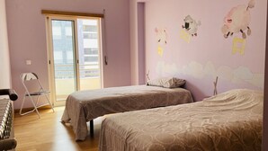 A bedroom with two beds, a chair, and a balcony. - Praia da Saude (Setúbal)