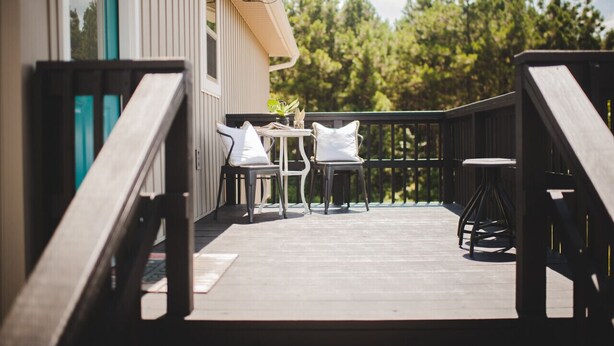 Une terrasse en bois avec un espace salon extérieur, comprenant des chaises et une table, donnant sur une zone boisée.