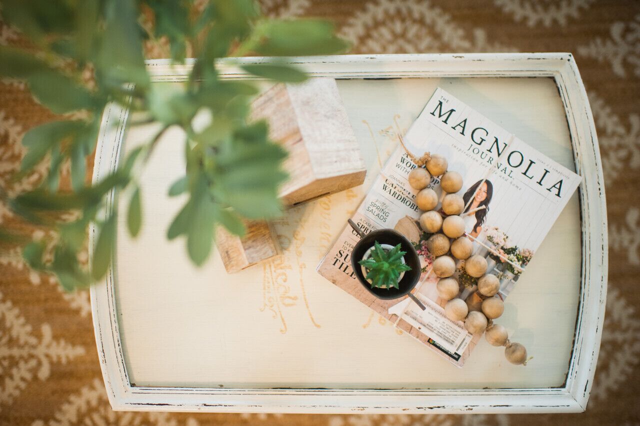 A white tray with a magazine titled 'The Magnolia Journal', a small potted plant, and some decorative items.