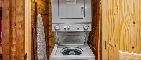A compact, wooden-walled laundry room with a built-in washer and dryer, a fire extinguisher, and a sign with instructions.