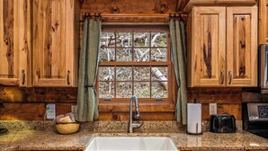 A kitchen with wooden cabinets, a granite countertop, a stainless steel sink, a Bosch dishwasher, and a window with curtains.