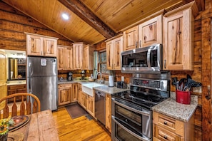 A wooden cabin interior with a kitchen featuring a stainless steel refrigerator, a microwave, a stove, and wooden cabinets.