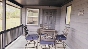 Varanda coberta com uma mesa e quatro cadeiras, uma porta e janelas.