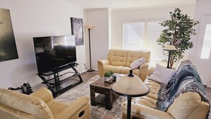 Uma sala de estar com televisão, dois sofás, uma mesa de centro e um abajur.