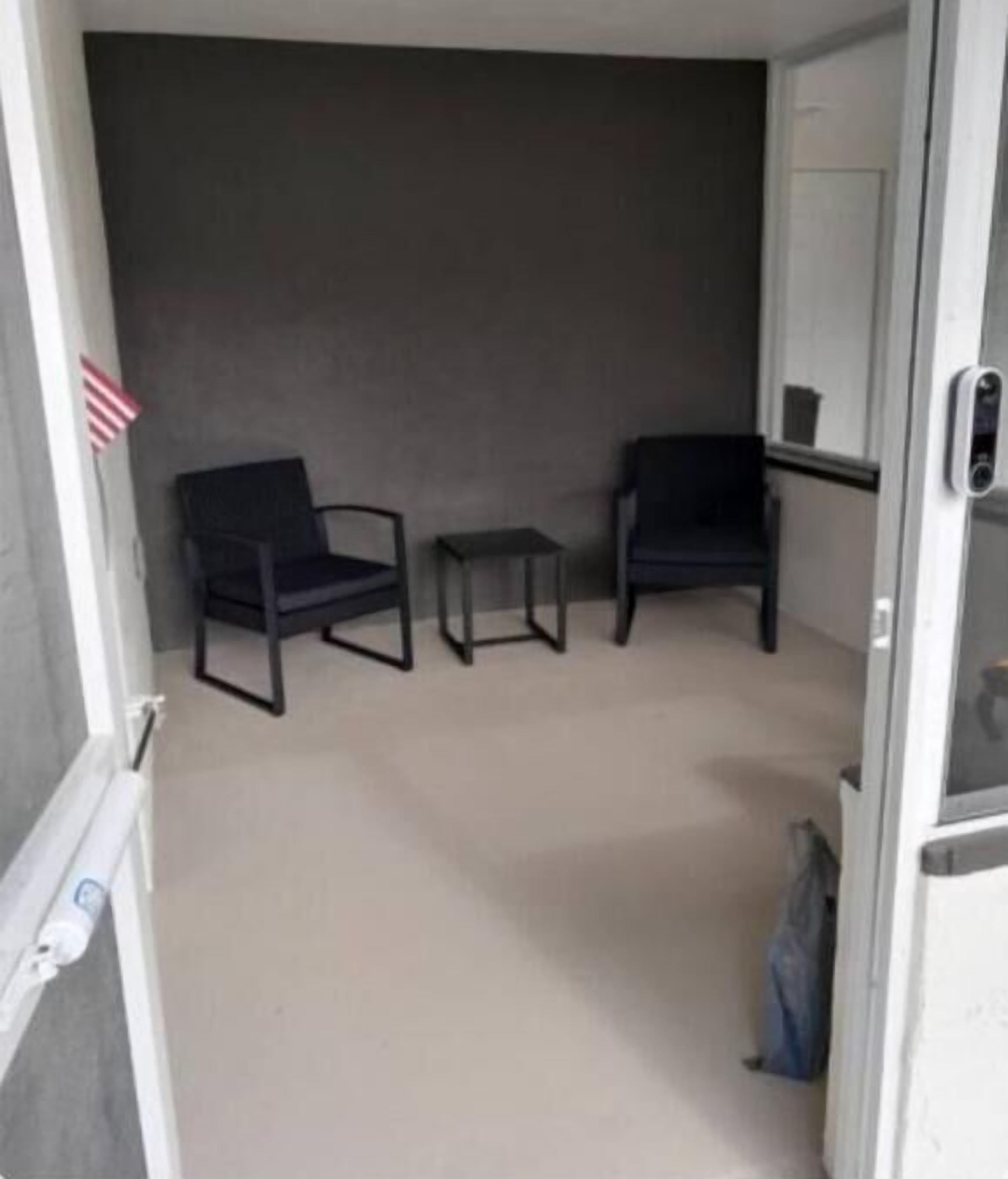 Une pièce avec deux chaises noires et une petite table, un mur gris et une porte blanche.