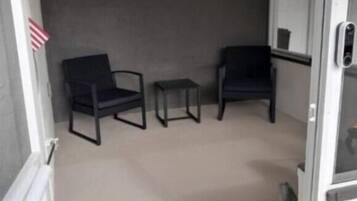 Une pièce avec deux chaises noires et une petite table, un mur gris et une porte blanche.