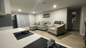 Ein modernes Wohnzimmer mit einem Ecksofa, einem Sessel und einem Blick auf den Küchenbereich im Hintergrund.