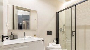A modern bathroom with a glass shower enclosure, a white sink with a mirror above, and a toilet with a towel on top. - Charming Studio for Two in Beautiful Chamberí (Madrid)