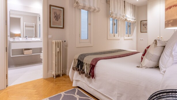 A bedroom with a bed, a bedside table, a radiator, a window with curtains, and a framed picture on the wall. - Elegant 2-Bed Apartment in Salamanca, Madrid (Madrid)