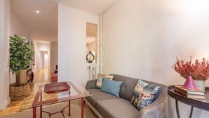 A modern living room with a glass coffee table, a grey sofa with patterned cushions, a potted plant, and a vase with dried flowers. - Elegant 2-Bed Apartment in Salamanca, Madrid (Madrid)