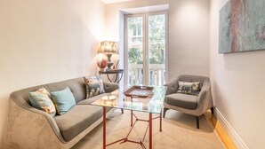 A modern living room with a glass coffee table, two grey sofas, a lamp, and a view through a glass door. - Elegant 2-Bed Apartment in Salamanca, Madrid (Madrid)