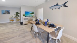 Un coin repas avec une table en bois, des chaises blanches et un poisson décoratif accroché au mur.