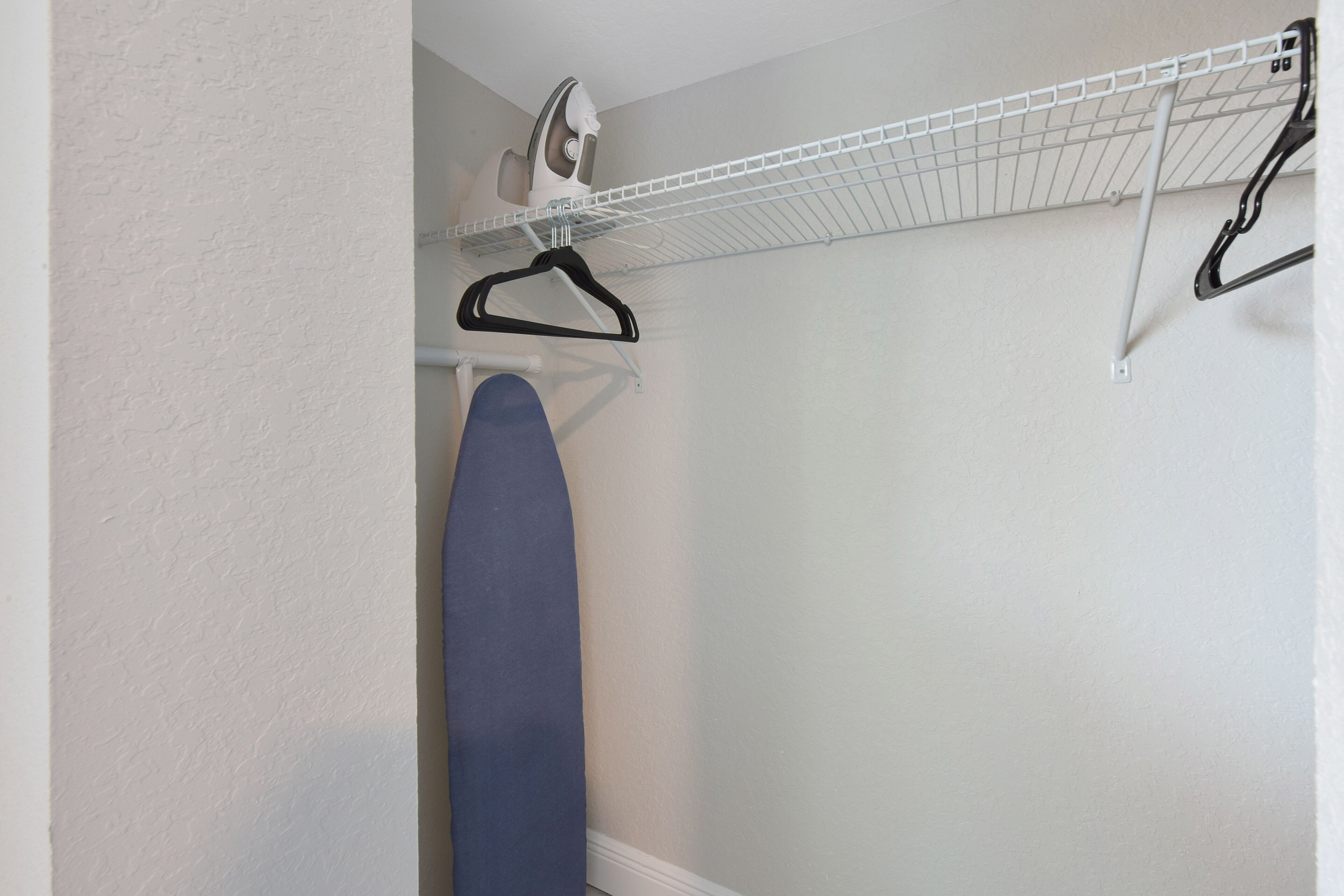 A laundry area with a hanging rack, an ironing board, and a wall-mounted iron.