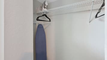 A laundry area with a hanging rack, an ironing board, and a wall-mounted iron.