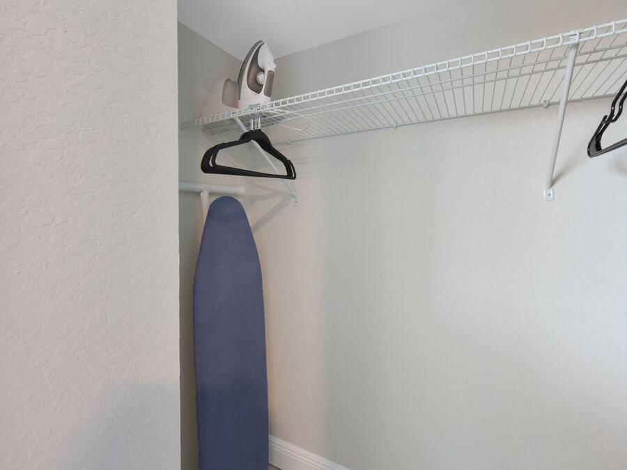 A laundry area with a hanging rack, an ironing board, and a wall-mounted iron.