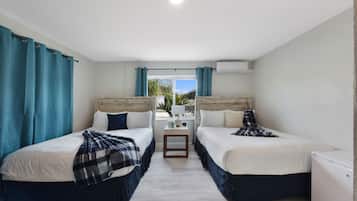 A hotel room with two beds, a small table, and an air conditioning unit.