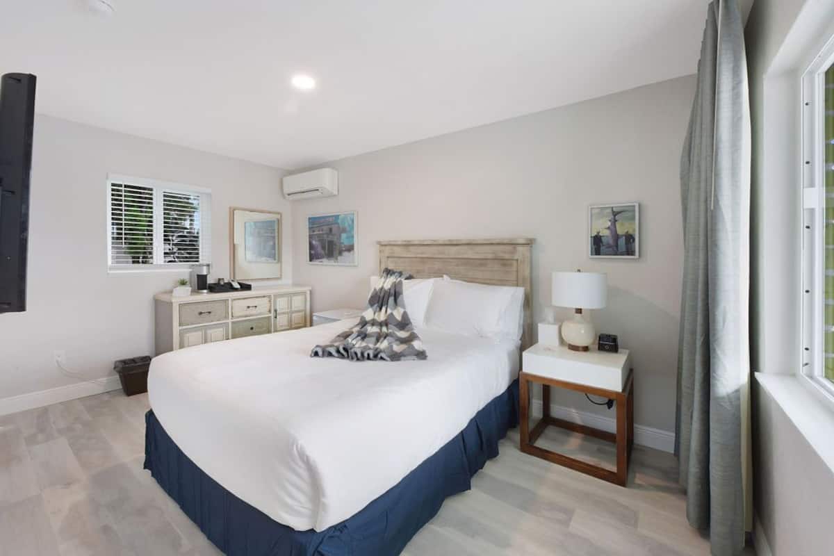 Une chambre à coucher bien rangée, avec un grand lit, des tables de chevet, une commode et des œuvres d’art accrochées aux murs.