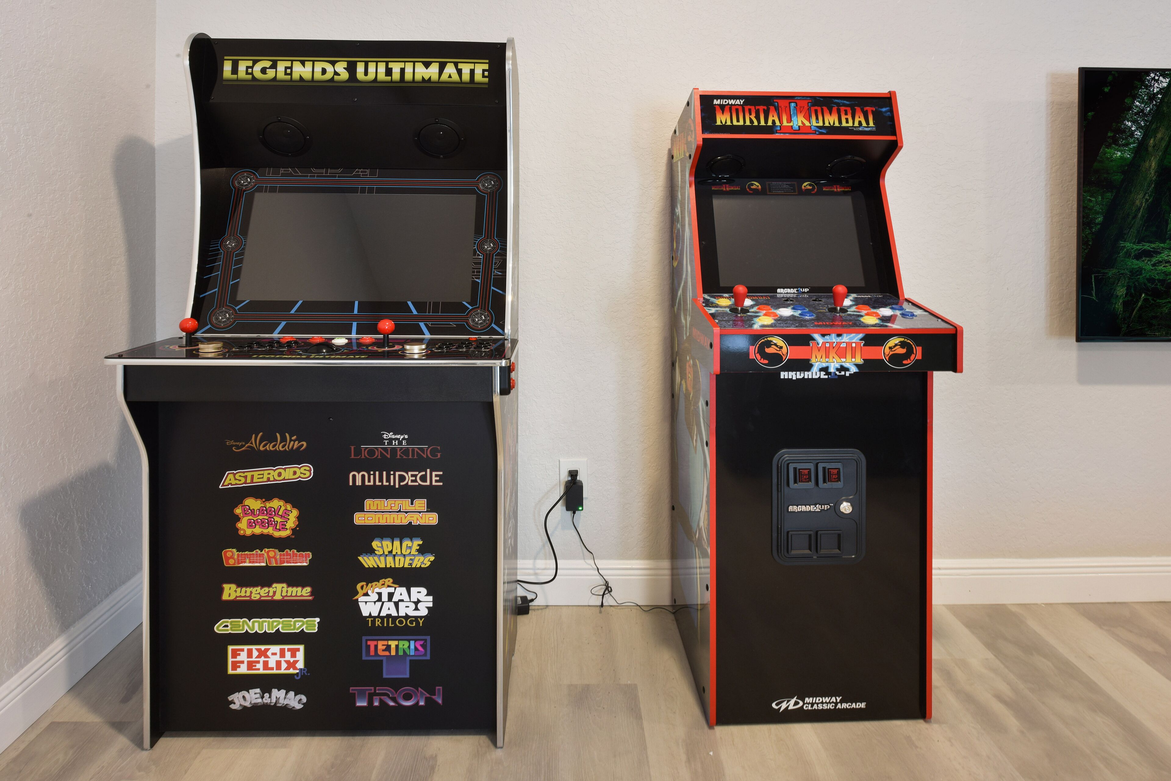 Two arcade machines, one labeled 'Legends Ultimate' and the other 'Midway Mortal Kombat', with various game titles listed on their sides.