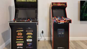 Duas máquinas de jogos de fliperama, uma com a inscrição 'Legends Ultimate' e outra com 'Midway Mortal Kombat', exibindo diversos títulos de jogos em suas laterais.