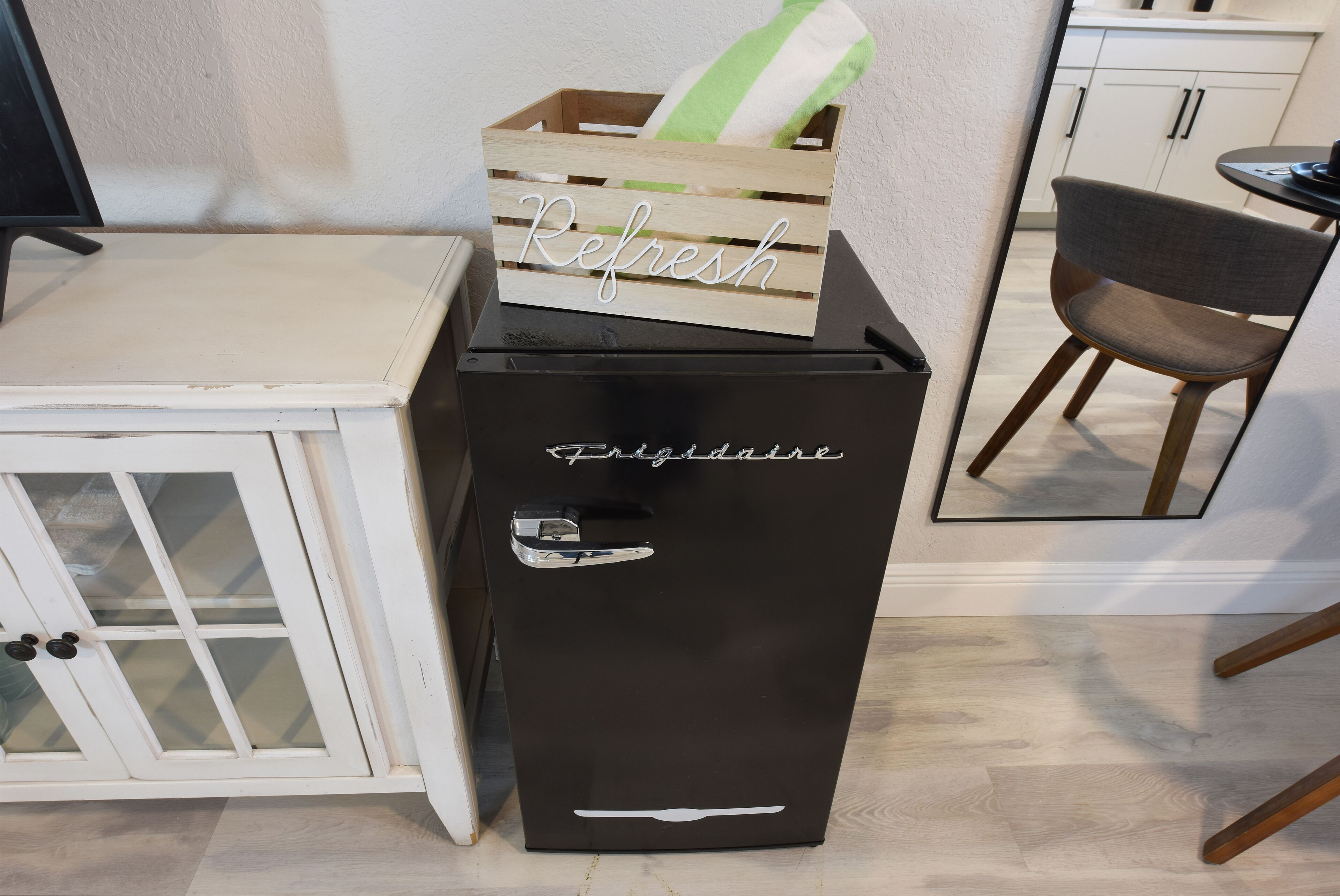 Ett svart kylskåp med ordet ”Refresh” på ovansidan och ”Frigidaire” på sidan, placerat bredvid ett vitt skåp med glasdörrar.