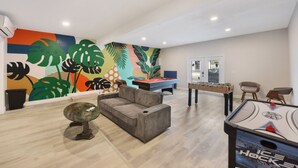 Un vaste espace de vie comprenant une table de billard, un baby-foot et une fresque murale aux couleurs vives.