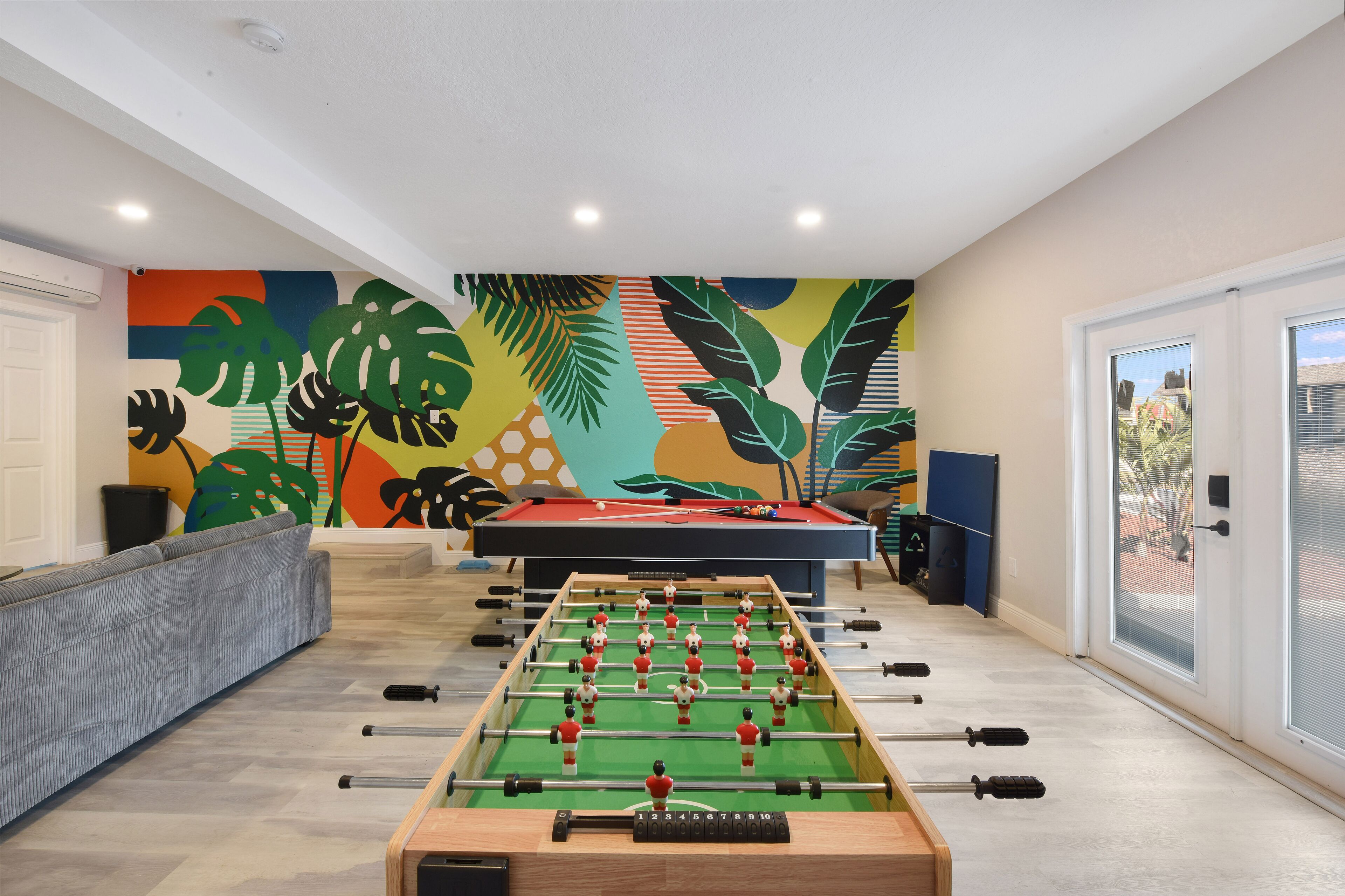 Une pièce avec une table de baby-foot, un canapé et une fresque murale colorée.