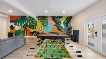 Une pièce avec une table de baby-foot, un canapé et une fresque murale colorée.