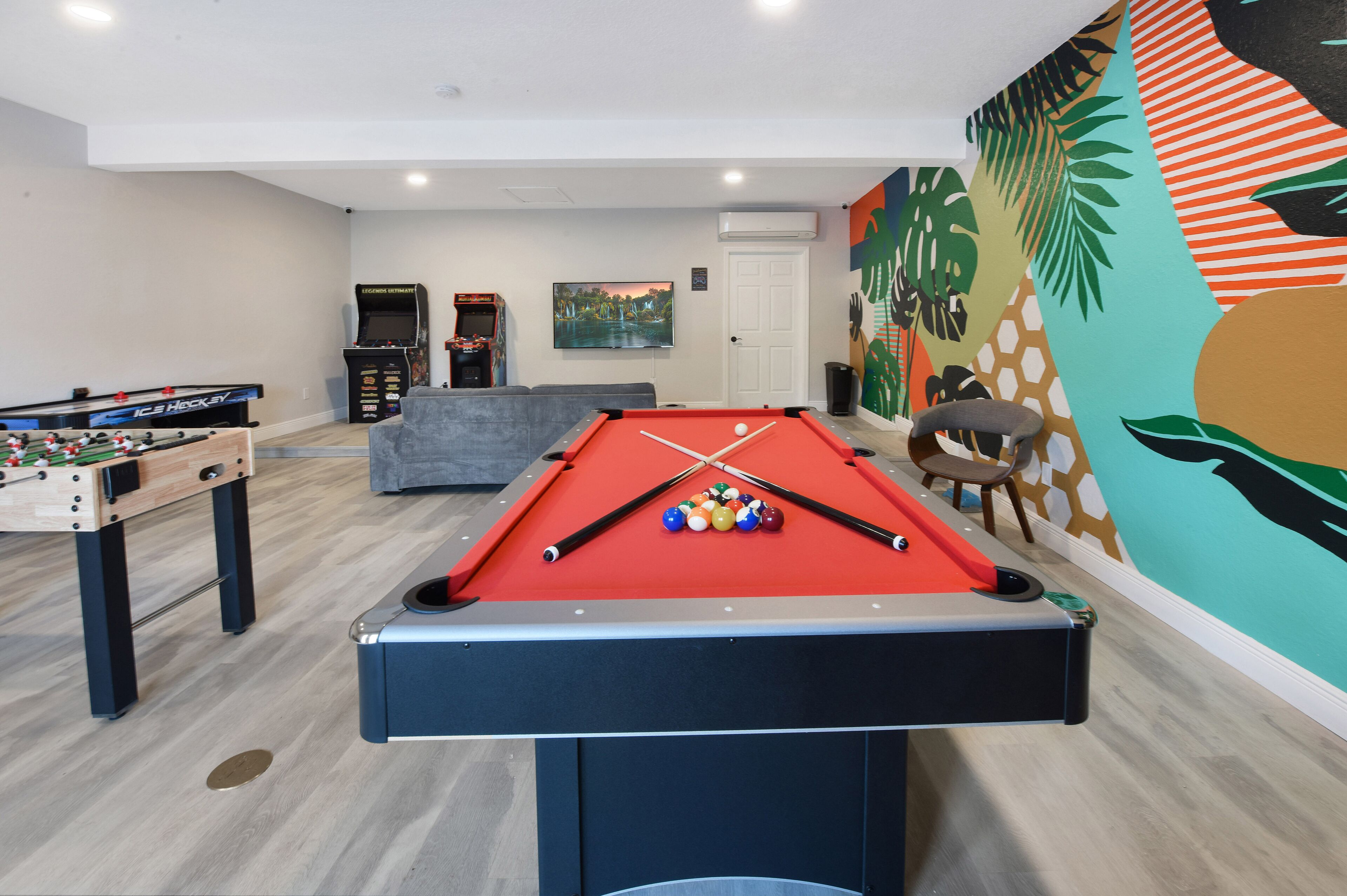 Una mesa de billar con bolas, una mesa de fútbol de mesa y un sofá en una sala con un mural.