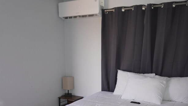 A neatly made bed with white bedding, a bedside table with a lamp, and an air conditioning unit mounted on the wall. - 068A Cozy Studio Grand Canyon South Rim Sleeps-2 (Williams)