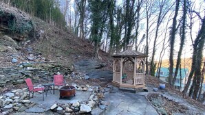Un patio de piedra con un brasero, sillas rojas y un gazebo de madera.