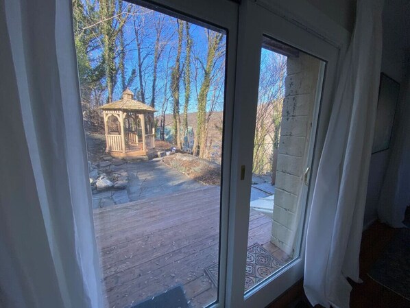 On aperçoit, à travers une porte vitrée, un espace extérieur agrémenté d’un belvédère, d’une terrasse en bois et d’un mur en briques.